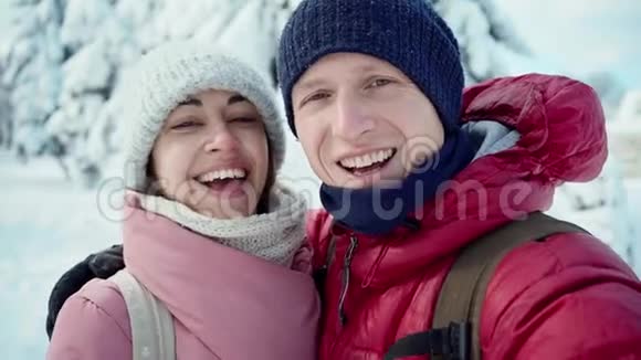 阳光明媚的冬日一对幸福微笑的年轻夫妇在白雪皑皑的冬季公园散步男人和女人很可爱视频的预览图