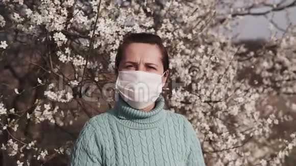 戴着医疗面具的年轻女子在一棵盛开的树的背景下视频的预览图