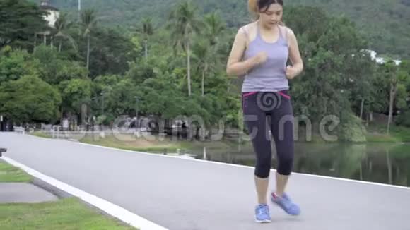 年轻健康的亚洲女人在公园晨跑时停下来系鞋带视频的预览图