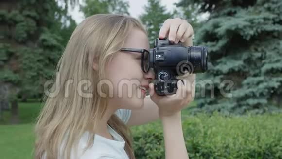 眼镜中漂亮的金发年轻女摄影师在公园拍照并在之前仔细评估结果视频的预览图