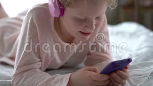 现代生活中的Z一代十几岁的女孩穿着睡衣戴着耳机在床上听着音乐视频的预览图