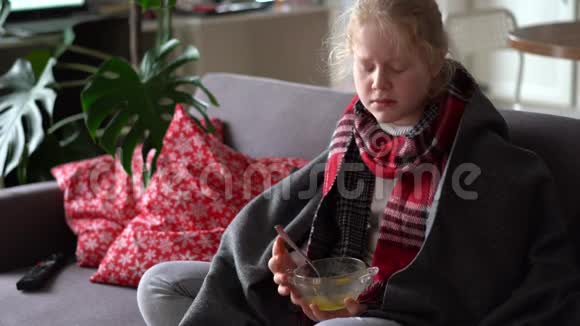 一个戴着围巾和格子的生病孩子的肖像女孩在公寓的沙发上吃肉汤视频的预览图
