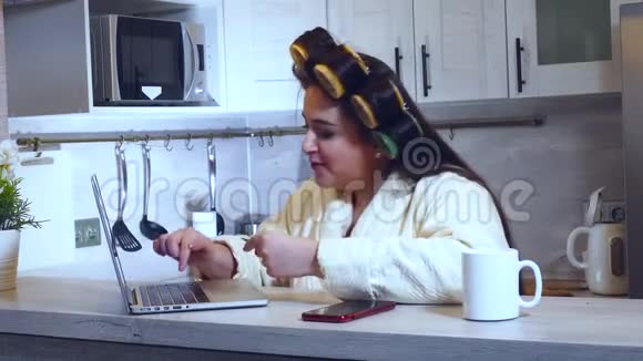 家庭主妇带卷发器使用笔记本电脑上网购物视频的预览图