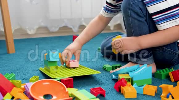 特写4k视频小托德勒男孩组装彩色玩具砖和块在蓝色地毯上的游戏室视频的预览图