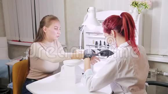 在美容院戴手套的女美甲师用湿毛巾擦拭顾客的指甲视频的预览图