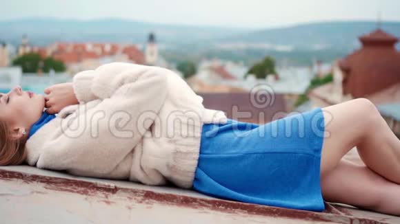 一位身穿白色环保毛皮的年轻女子躺在屋顶上视频的预览图