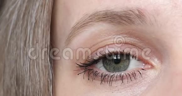 女人特写镜头灰绿色的雌性眼睛在镜头前闪烁视频的预览图