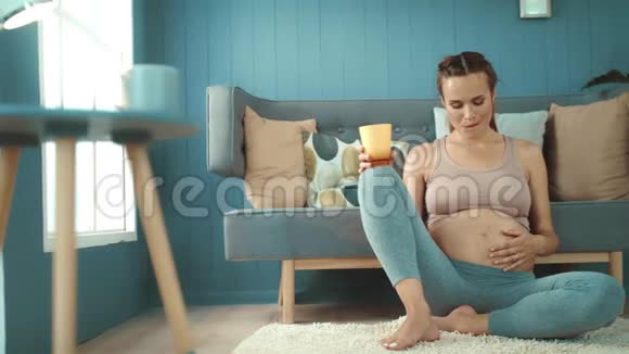 特写年轻孕妇坐在家里的地板上做瑜伽姿势视频的预览图