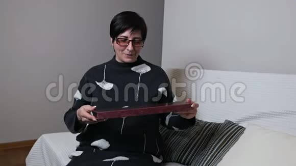 一位老妇人很高兴收到一份礼物幸福的老妇人拿着一个盒子坐在客厅的沙发上视频的预览图