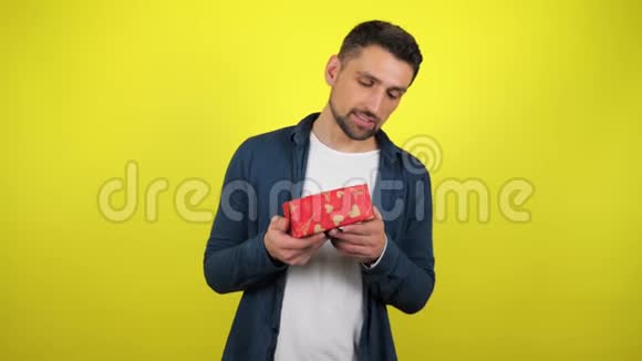 一个穿着白色T恤的年轻人欣赏手里拿着礼物的盒子微笑着看着相机视频的预览图