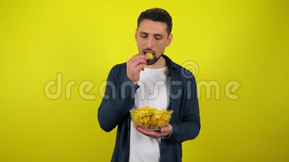 一个穿着蓝色衬衫和白色T恤的年轻人正在看着相机吃着透明玻璃盘子里的薯片视频的预览图
