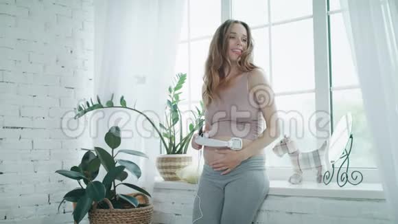 微笑的孕妇听音乐与耳机在现代家庭视频的预览图