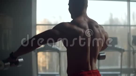 一个没有t恤的人把哑铃举到窗前做肩部肌肉锻炼健美运动员视频的预览图