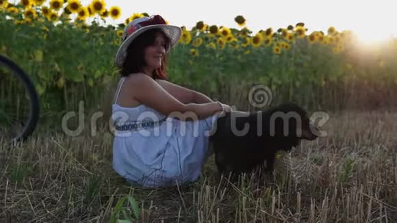 一个戴着帽子穿着白色裙子的女人坐在割草场上视频的预览图