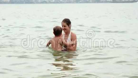 4K镜头快乐的微笑母亲和她的小儿子在海洋游泳时玩得开心和拥抱视频的预览图