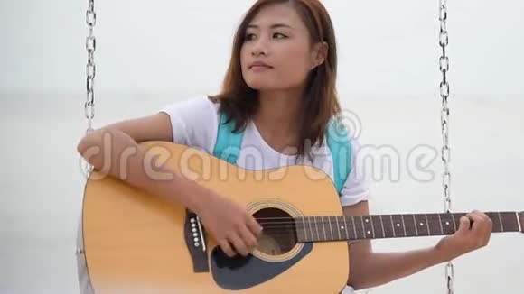 美丽的亚洲可爱女孩在海滩上弹声吉他女人穿着卡苏克白色t恤坐在热带海滩夏天我视频的预览图