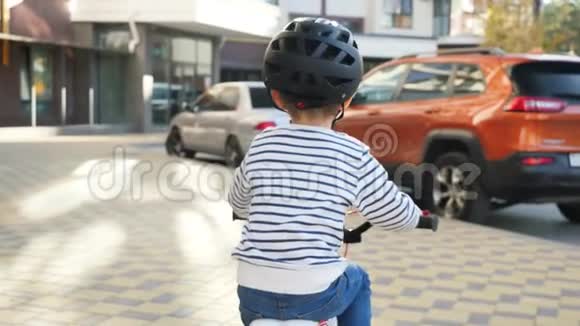 特写4k视频戴防护头盔的小男孩骑自行车在城市街道上视频的预览图