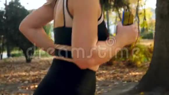 在公园慢跑时年轻的运动女性手持智能手机的特写视频视频的预览图
