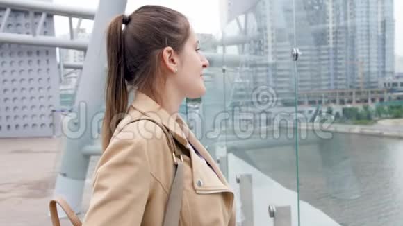 4k视频年轻微笑的女人站在屋顶看着河上的天际线和摩天大楼视频的预览图