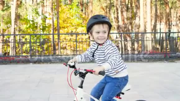 4k视频可爱的男孩戴着防护头盔在街上骑自行车时笑着笑视频的预览图