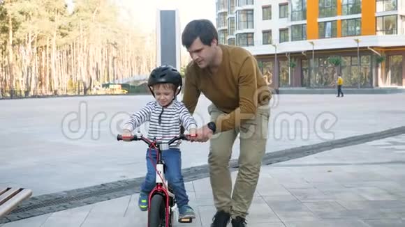 快乐的年轻父亲教他的小儿子骑自行车和支持他的4K镜头视频的预览图