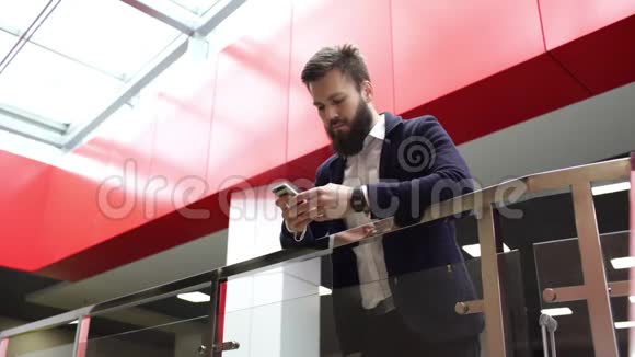近距离观看平静留胡子的男人在手机上打字同时靠在玻璃栅栏上站在现代视频的预览图