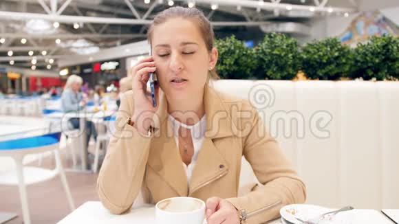 4k视频年轻自信的女人坐在购物中心的咖啡厅边打电话边喝咖啡视频的预览图