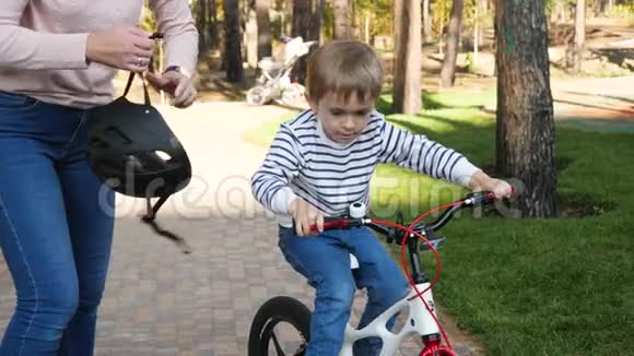 4K录像显示小男孩骑着自行车坐在公园里而他的母亲则戴着保护头盔视频的预览图