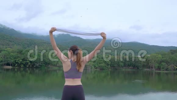 年轻健康的亚洲女人在户外自然公园晨练时手里拿着白毛巾伸着胳膊视频的预览图