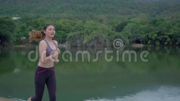 一位年轻健康的亚洲妇女在一个有湖和山景的当地公园晨练时动作视频的预览图