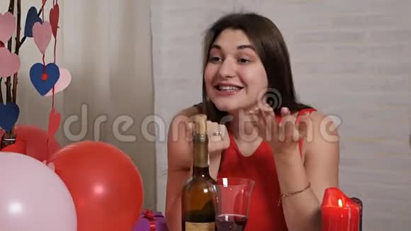 一个身穿红裙的漂亮女孩在餐桌上喝着酒杯里的酒端着巧克力和她交流视频的预览图