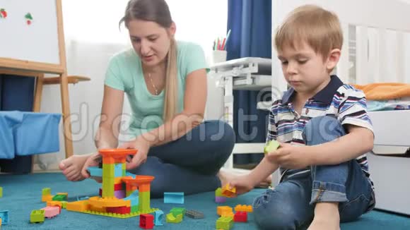 4k视频小男孩和妈妈一起在卧室的地板上搭建一座五颜六色的砖块和积木塔视频的预览图