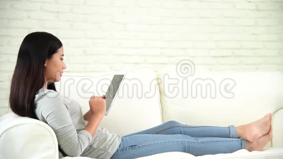 亚洲女性在智能手机上使用智能平板购物在线网站在温暖的家舒适的沙发上有笑脸视频的预览图