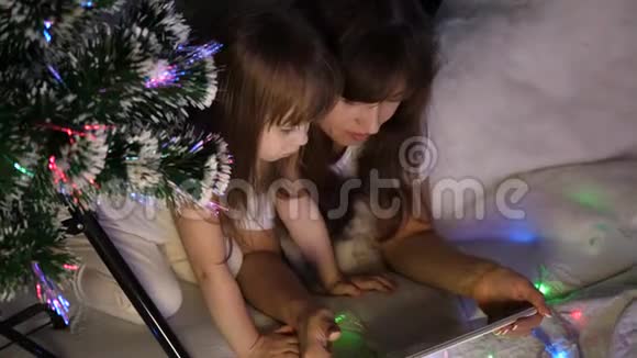 圣诞节晚上妈妈和女儿在平板电脑上玩和看动画片在一个带花环帐篷里的孩子房间里视频的预览图