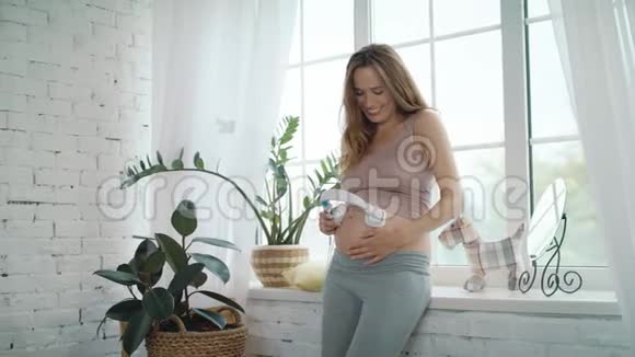 把欢快的孕妈妈贴在家里的肚子上耳机视频的预览图