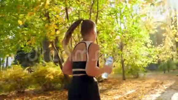 4K慢动作视频美丽的年轻女子在秋公园慢跑和运动时从瓶子里喝水视频的预览图
