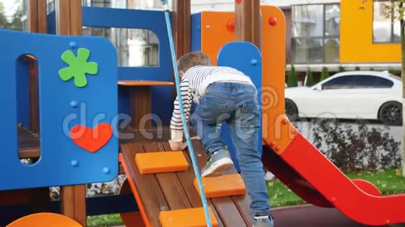 快乐微笑的小男孩在五颜六色的木制操场上攀爬和玩耍视频的预览图
