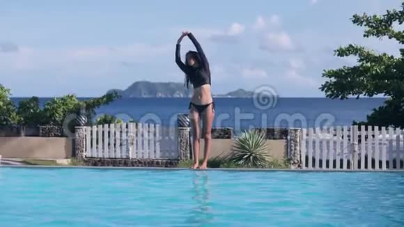 亚洲女孩做伸展运动在海山背景的游泳池里潜水视频的预览图