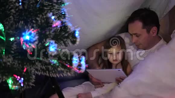 家庭圣诞节的概念孩子们和爸爸在圣诞节晚上玩平板电脑在孩子们房间里在帐篷里和视频的预览图
