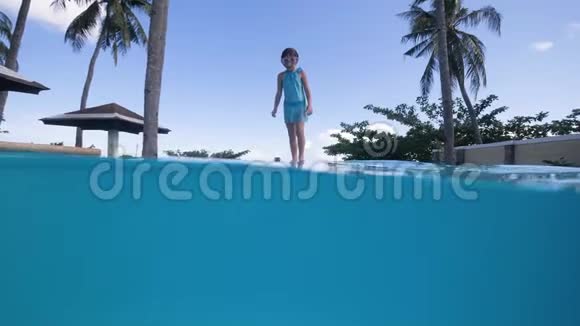 戴着游泳面具的小女孩在游泳池里跳跃在热带慢动作洗澡视频的预览图