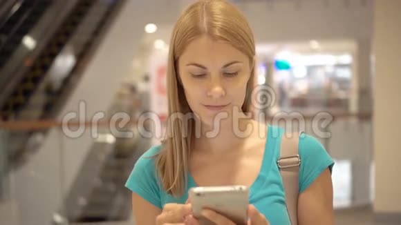 年轻女子站在购物中心用智能手机浏览阅读新闻与朋友聊天视频的预览图