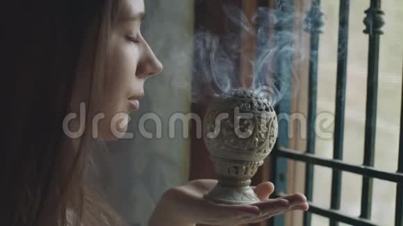 寺庙内闻着印度香炉白烟的年轻女子侧面画像带着秘密冥想的进攻性女孩视频的预览图