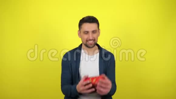 一个穿着白色T恤的年轻人拿着一个盒子手里拿着一件礼物看着相机微笑着黄色的背景视频的预览图