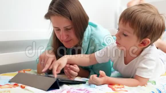 4k小男孩妈妈躺在床上玩电子游戏的数码平板电脑特写视频视频的预览图