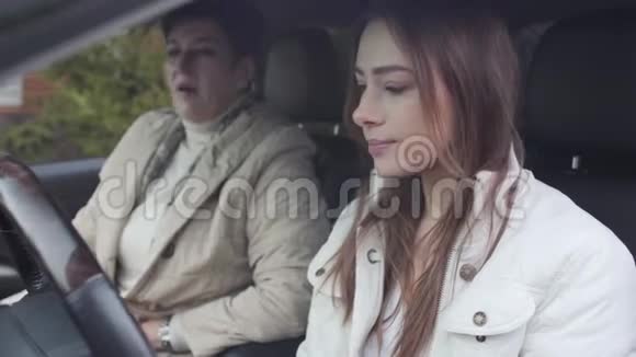 兴奋的白种人女孩坐在司机座位上听聪明的女人解释如何开车的肖像快乐视频的预览图