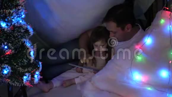 女儿和爸爸在圣诞节晚上玩平板电脑在孩子们房间的花环家庭圣诞节的概念儿童视频的预览图