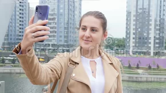 4k视频美丽微笑的年轻女子站在屋顶上用智能手机对着视频的预览图