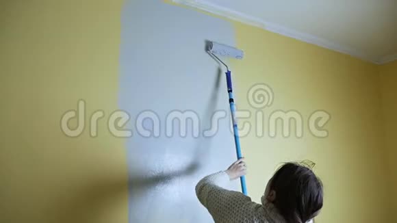 快乐的自学女孩用一个建筑滚筒画一堵黄色的墙和灰色的油漆独立公寓维修视频的预览图