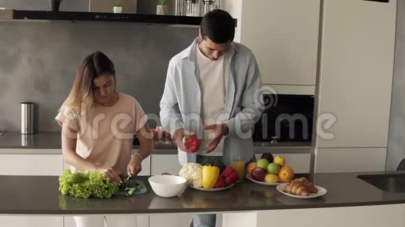 一对年轻的家庭情侣切鲜菜色拉在现代阁楼内部厨房一起做有趣的烹饪视频的预览图