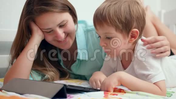 4k小男孩的特写镜头年轻妈妈躺在床上用数码电脑看动画片视频的预览图